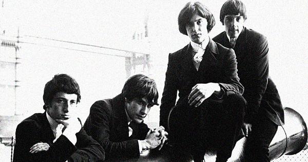 Image in QuizMyDay Ultimate Kinks Trivia: Hits, History & Facts Now trivia quiz featuring A 1964 promotional photograph of the Kinks. London's Tower Bridge is in the background.<br>In band biographer Doug Hinman's 2004 book <i>All Day and All of the Night</i>, p. 31, he dates this photograph to around August 2, 1964. He further writes: "It is likely that classic red-hunting-jacket shots with The Kinks in various poses around the Tower Of London [<i>sic</i>] and sitting on a cannon are taken at this time. They are used extensively in early promotional material. The session may well have been at the urging of new press officer Brian Sommerville upon the launch of his campaign to smarten up the band's image. Also, Summerville seeks to represent them as symbols of Englishness, a notion that will in time sell well to the American market."