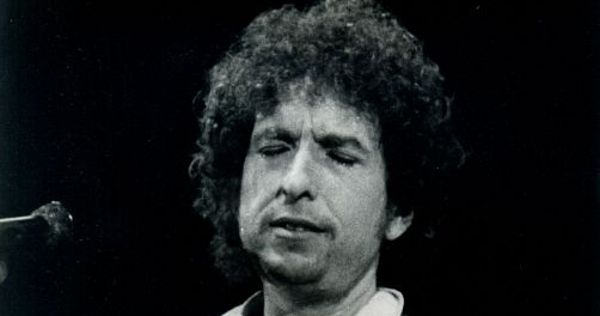 Image in QuizMyDay Knocking on Heaven's Door Song Quiz: Test Your Rock Expertise trivia quiz featuring Bob Dylan performing live onstage at Mini Estadi in Barcelona in 1984.