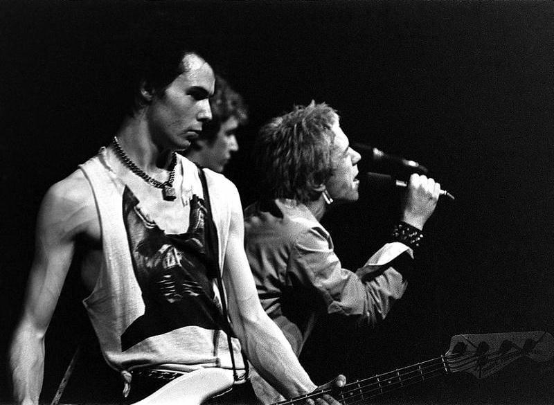 A Black and White picture of the Sex Pistols singing to microphone and playing electric guitars during a concert. This is the header picture for the Punk music QuizMyDay category